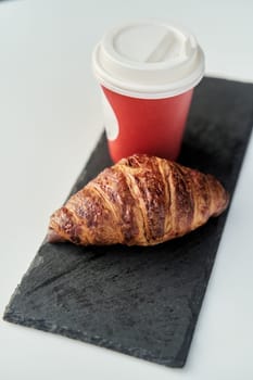 Red cup with coffee and a croissant on a table in a cafe. Morning breakfast. High-quality photo
