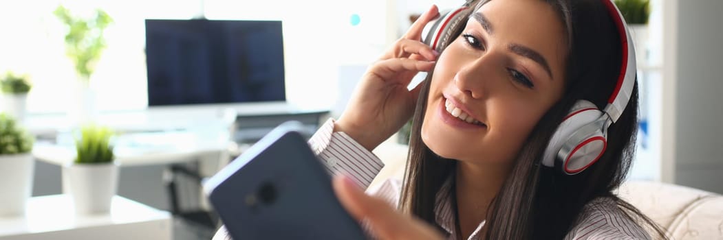 Beautiful woman in headphones holding smartphone at home. Applications for listening to quality music on your phone