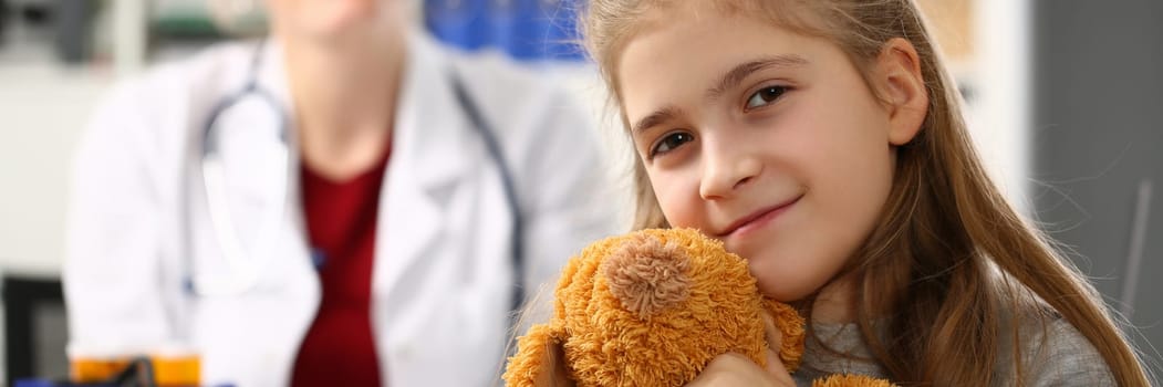 Little girl holding bear toy at medical appointment with pediatrician. Children doctor and child examination concept