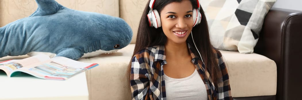 Young beautiful african american woman relaxing and listening to music with headphones on floor. Freelancer working remotely sitting at home with laptop concept