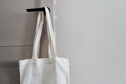 Eco friendly concept with white canvas tote bag hanging on door knob with two toned colored, Eco blank shopping sack with free copy space, Reduce plastic bags to reduce global warming. Canvas tote bag