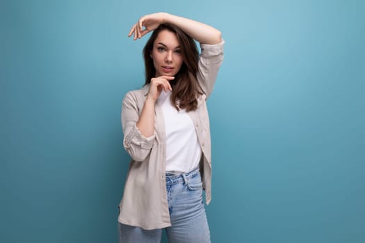 European model appearance young dark-haired lady in informal clothes posing against a blue background.