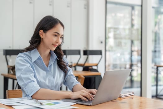 Portrait of beautiful smiling young businesswoman sitting at office bright modern work and typing on laptop.