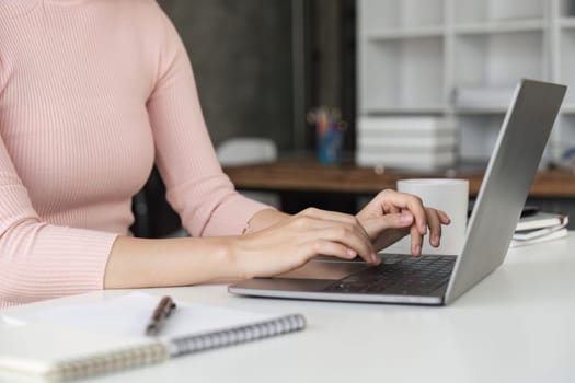 Woman sitting at desk and working at computer hands close up.