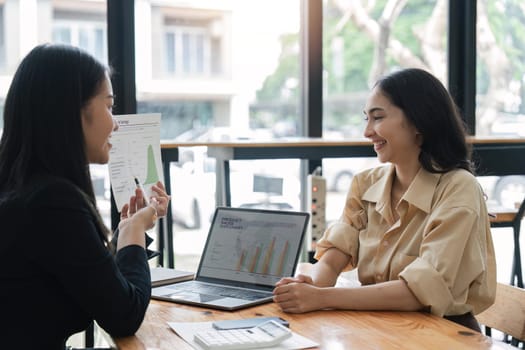 Two young businesswoman meeting and discussing about new business project plan, using computer analyzing financial and marketing with happiness at office.