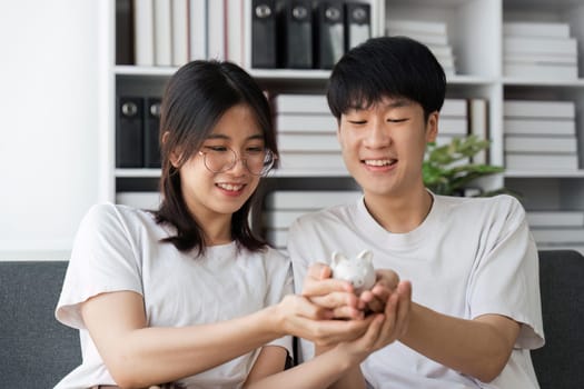 Smiling, happy young family together put coins in piggy bank to save money. Married couple are planning to save up finances. Savings, investments, financial freedom, business, hope for success.