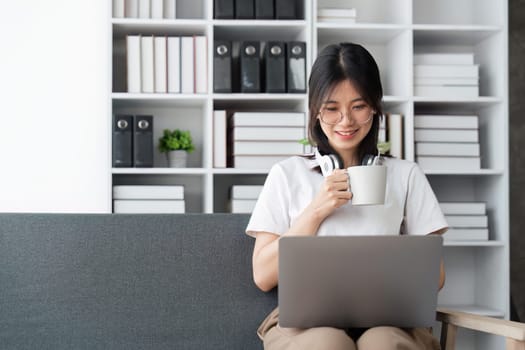 Beautiful young woman working on laptop computer while sitting at the living room, drinking coffee.