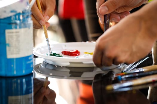 Close-up of hands with brushes mixing paints on a palette at a workshop.