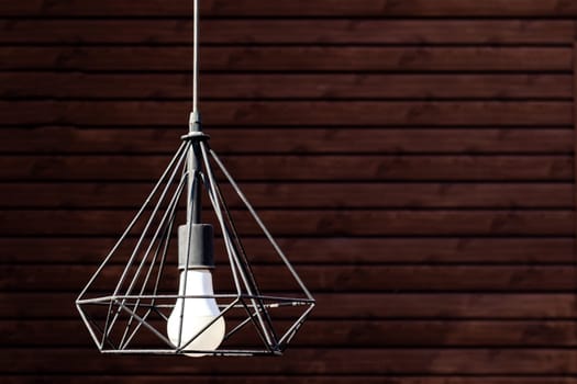 Close-up of modern pendant lamp hanging during on wooden wall background, copy space.