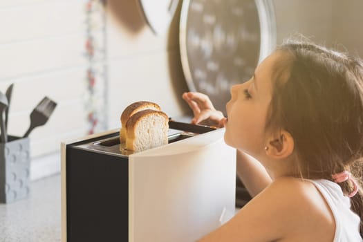 Caucasian girl 5 -7 years old cooks breakfast from toast in a toaster in a home kitchen, life style.