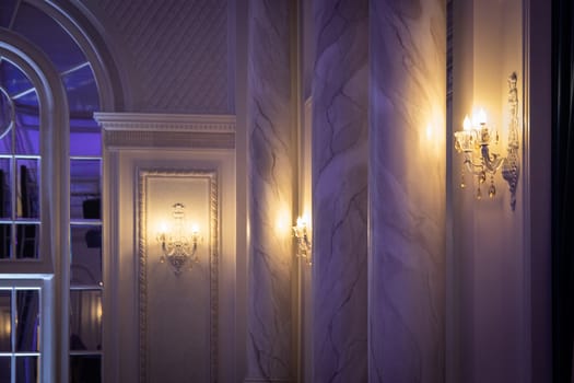 Part of the interior of the hall in a classic style with luminous sconces on the walls.