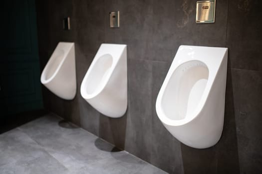 Three white urinals hanging on the wall in a dark luxury public toilet.