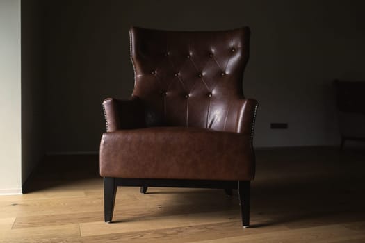 Brown leather armchair in an empty dark room by the window.