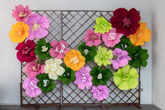 Large and small multi-colored paper flowers on a stand for a photo zone.