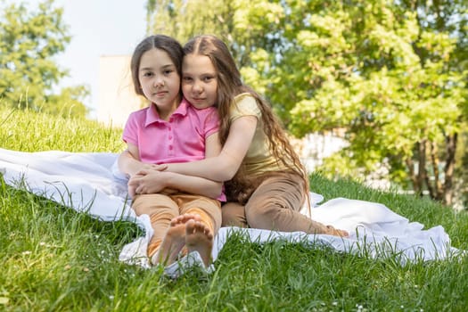 Two Little Girls, Sisters With Long Hair Sits Hugging On Grass in Meadow At Sunny Day. Caucasian Asian Siblings, Love And Care, True Friendship. Horizontal Plane. High quality photo