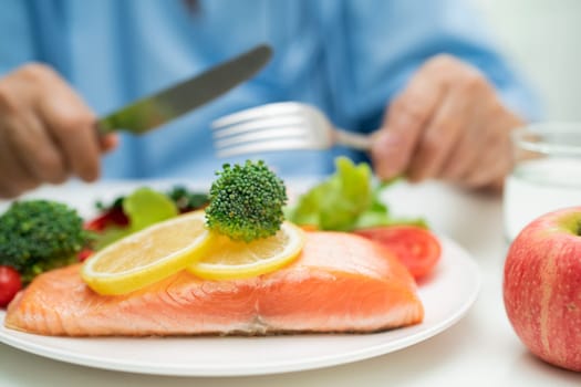 Asian elderly woman patient eating salmon steak breakfast with vegetable healthy food in hospital.