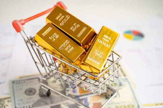 Gold bar in shopping cart on US dollar banknotes money and graph, economy finance exchange trade investment concept.