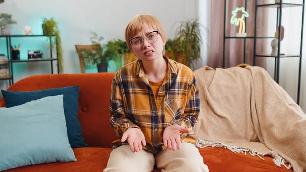 What. Why. Woman raising hands in indignant expression asking reason of failure demonstrating disbelief irritation by troubles at modern home apartment. Portrait of girl in living room sitting on sofa