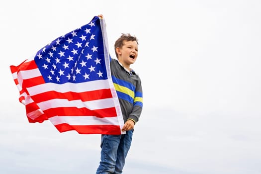Emotional portrait of patriotic american boy holding USA flag waving in the wind. Patriotic holiday. USA celebrate 4th of July.