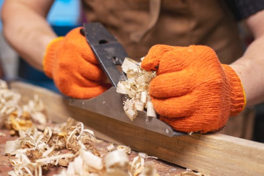 Carpenter's hands planing a plank of wood with a hand plane, workplace.