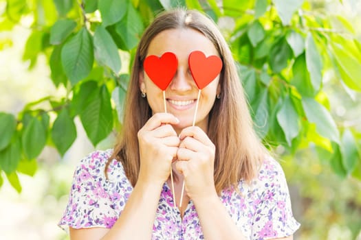 Happy beautiful woman closes her eyes with decorative hearts on the natural backround.