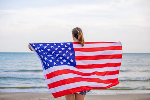 Back view of young woman holding national American flag on a ocean beach. USA Memorial day and Independence day concept.