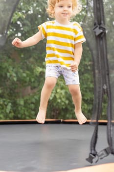 Child is jumping on a big trampoline outdoors in a park. Children outdoors activity.