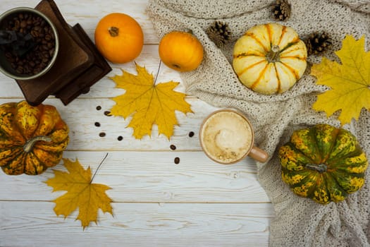 A variety of pumpkins, autumn yellow leaves and a mechanical coffee grinder are lying on a wooden table.