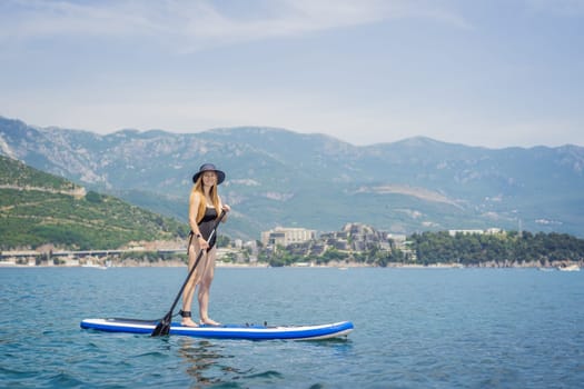 Young women Having Fun Stand Up Paddling in blue water sea in Montenegro. Against the backdrop of the Montenegrin mountains. SUP.