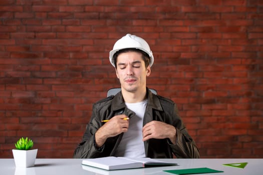 front view displeased male engineer sitting behind his working place and writing notes document plan business corporate property builder contractor agenda