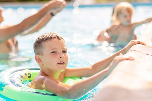 Funny happy child boy in swimming pool on inflatable rubber circle ring. Kid playing in pool. Summer holidays and vacation concept.