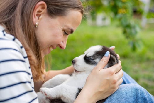 Beautiful woman in a striped t-shirt happily plays with a small husky puppy in the park outdoors.