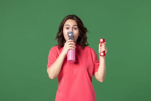 front view young saleswoman drinking from thermos and holding dumbbell on green background job color yoga uniform athlete shopping workout body work