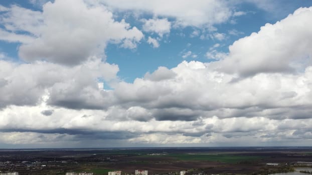 Fast movement of white cumulus clouds in blue sky during strong wind during day. Timelapse. Aerial drone view. Panoramic natural background. Rain. Rainy cloudy weather. Cloudscape. Scenic landscape.