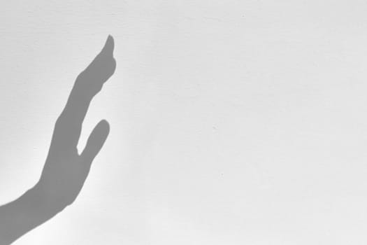 Shadow silhouette of hand raised in form of stop gesture, on gray background, copy space, noise