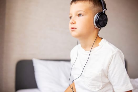 A boy in white T-shirt on the bed at home playing with pc tablet or reading online and listening to music with headphones.