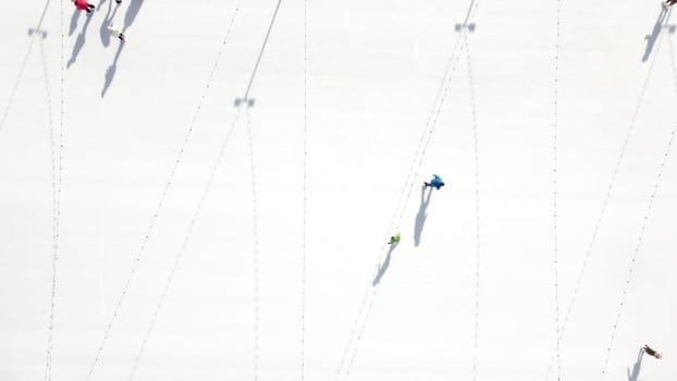 People ride on white ice rink on street and cast long shadows. People skating on sunny winter day. Top view. Aerial drone view. Leisure entertainment vacation weekend holidays activities lifestyle.