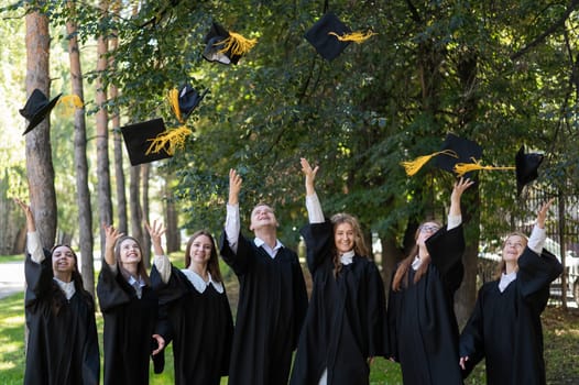 Classmates in graduation gowns throwing hats outdoors