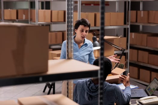 Diverse warehouse employees discussing transportation logistics problem while preparing customer packages, working in storehouse delivery department. Workers preparing online orders