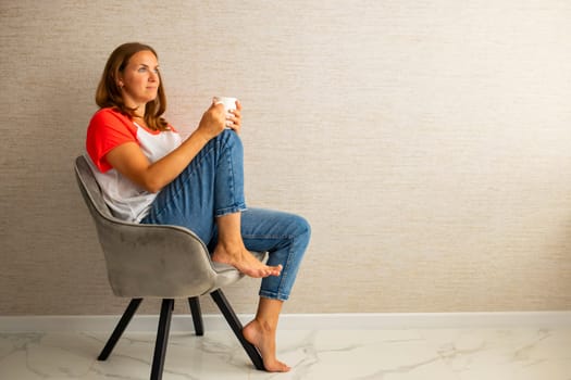 Young beautiful woman in casual wear sitting in armchair with cup of hot coffee. Happy woman relaxing in armchair. Banner with copy space.