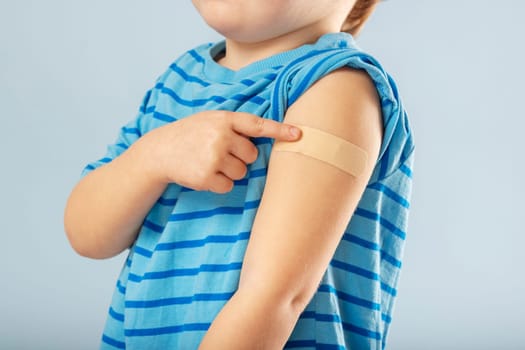 Vaccination of children. Vaccinated kid boy showing arm with adhesive bandage after vaccine injection. Kids and covid-19 prevention, antiviral immunization.