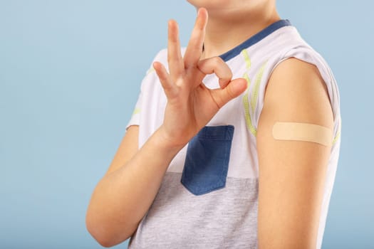 Vaccination of children. Happy vaccinated kid boy is gesturing okay and showing arm with adhesive bandage after vaccine injection. Kids and covid-19 prevention, antiviral immunization.