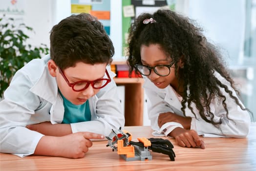 Engineering, learning and children building a robot hand together in a classroom at school and being curious. Clever, education and young engineer students working in a science class doing research.