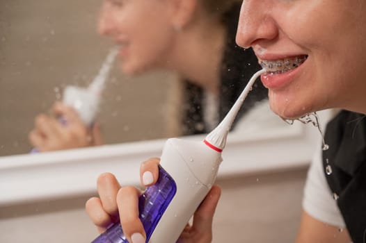 A woman with braces on her teeth uses an irrigator. Close-up portrait