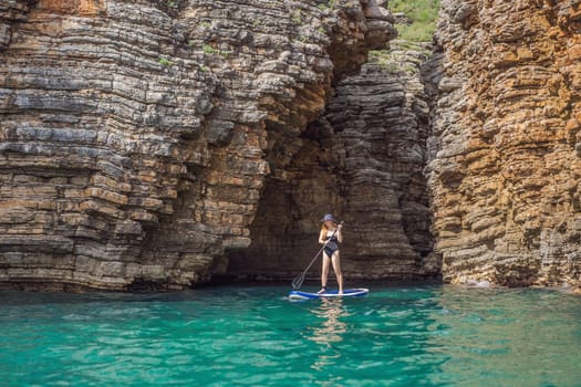 Young women Having Fun Stand Up Paddling in blue water seaamong the rocks in Montenegro. SUP.