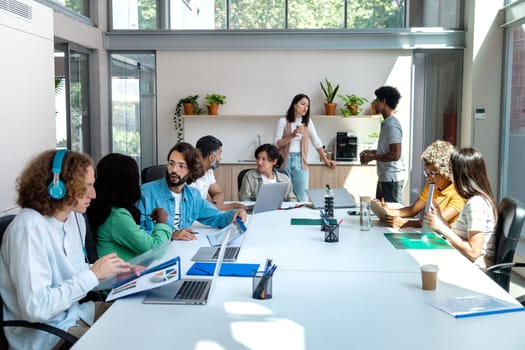 Multiracial group of coworkers share big table in spacious bright coworking space. Copy space. Business concept. Startup concept.