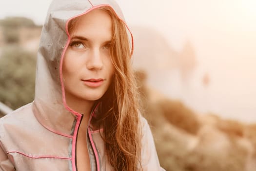 Woman rain park. Happy woman portrait wearing a raincoat with transparent umbrella outdoors on rainy day in park near sea. Girl on the nature on rainy overcast day