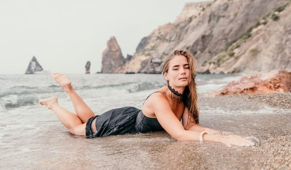 Woman travel sea. Young Happy woman in a long red dress posing on a beach near the sea on background of volcanic rocks, like in Iceland, sharing travel adventure journey