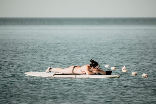 Sea woman sup. Silhouette of happy middle aged woman in rainbow bikini, surfing on SUP board, confident paddling through water surface. Idyllic sunset. Active lifestyle at sea or river