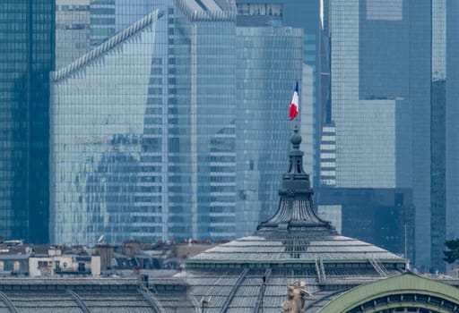 6 May 2023 Paris, France. The French flag is prominently displayed atop the Grand Palais with the modern day skyline of La Defense in the background. The Grand Palais will be a venue for the Paris 2024 Olympic games hosting fencing and Taekwondo.